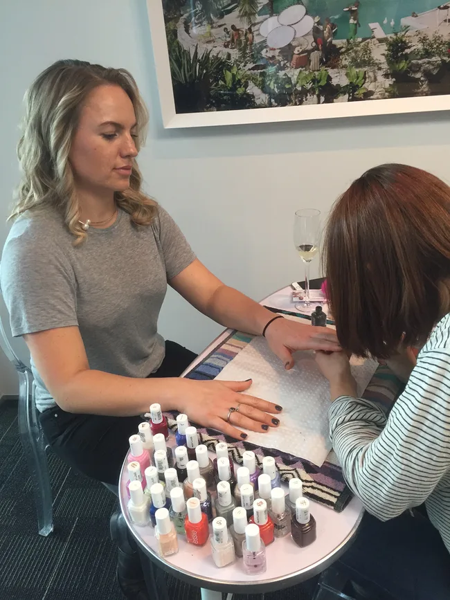 Woman getting a manicure at a table with various nail polish bottles.