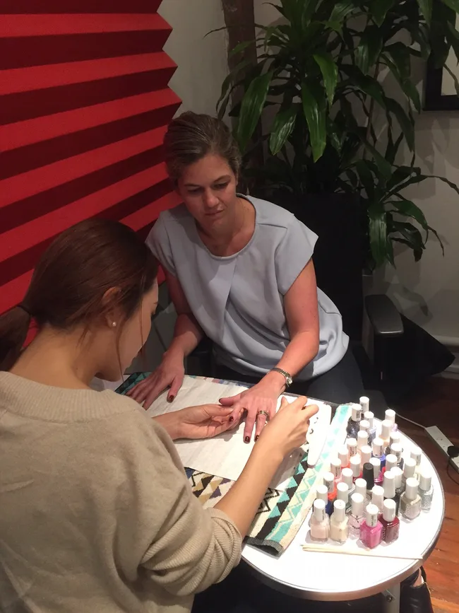 A woman is getting a manicure at a table with various nail polish colors and tools.