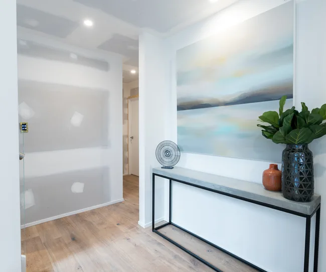 Modern hallway with large abstract painting, decorative fan, and vases on a console table, with light wood flooring.