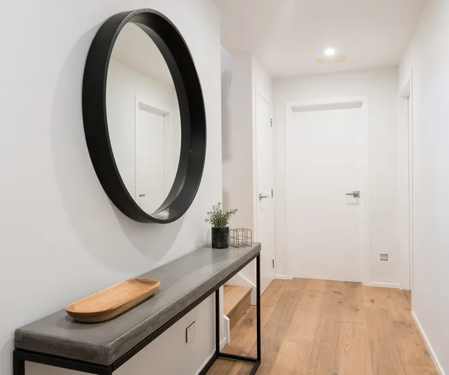 Modern hallway with wooden floor, round mirror, and a minimalist console table holding a wooden tray and small plant.