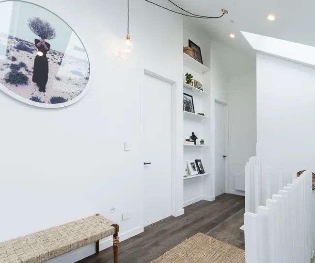 Modern white hallway with a round wall art, bench, shelves, and wooden flooring.