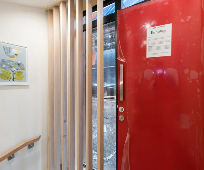 Red door with quality check notice, next to wooden slats and artwork showing blue flowers and a bird.