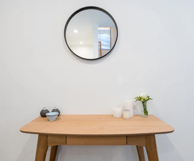 Wooden table with vases and candles beneath a round wall mirror.