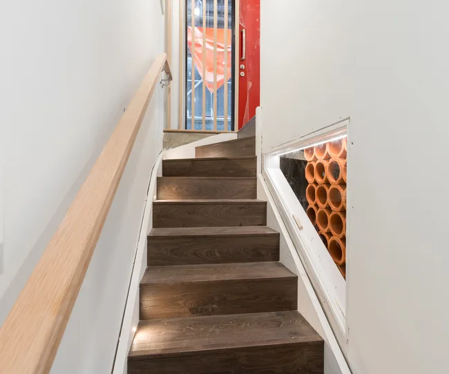 Wooden staircase with a metal handrail, glass-paneled wall, and orange construction cones outside a window.