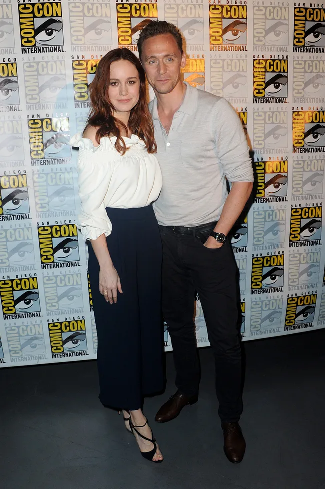 A man and woman pose together at San Diego Comic-Con, against a backdrop with the event's logo.