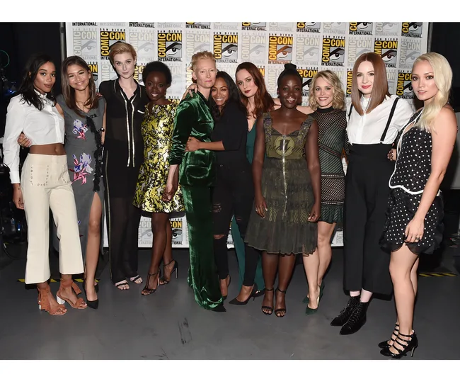 Group photo of ten women posing together at San Diego Comic-Con with Comic-Con banners in the background.
