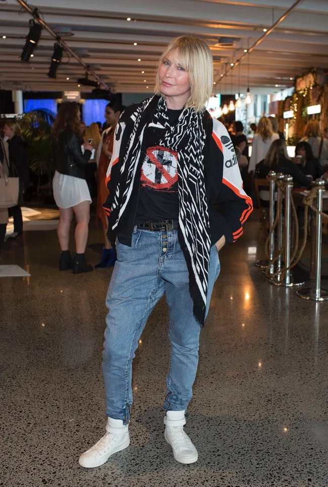 Person in casual outfit with a scarf, jeans, and sneakers, standing indoors at an event.