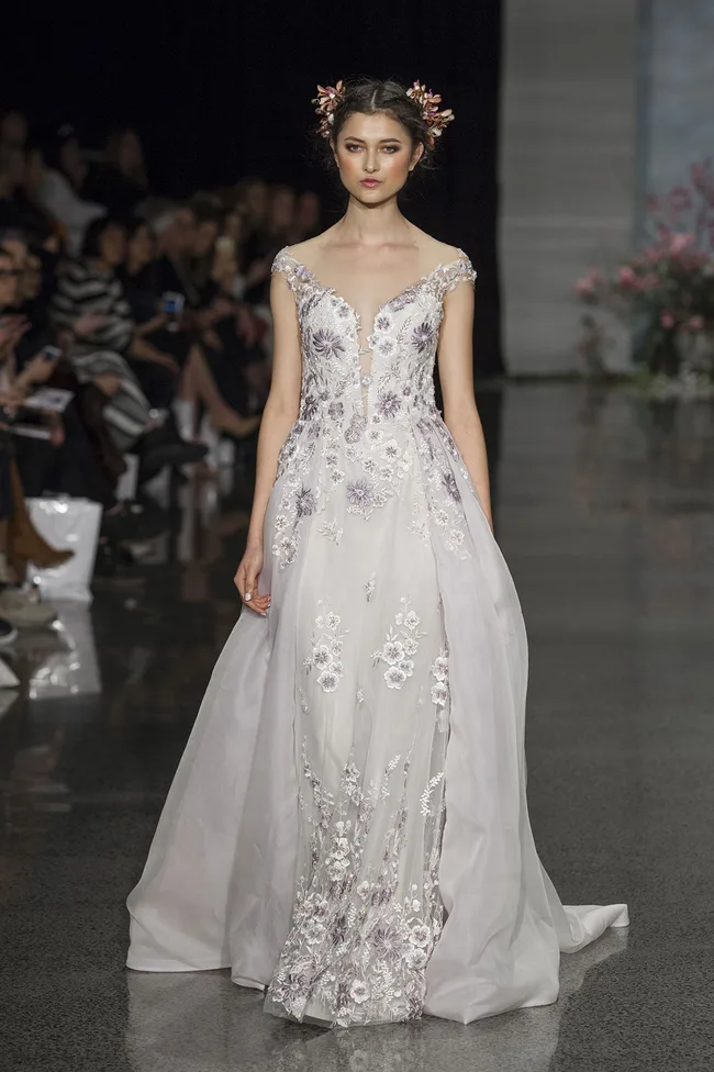 A model walks the runway in a floral embroidered white gown with floral headpiece at a fashion show.