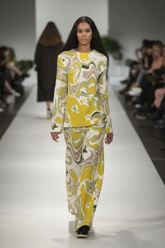 Model in a colorful abstract print outfit walks down a runway at a fashion show.