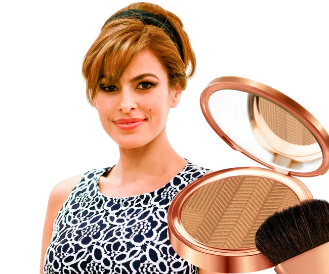 A woman with auburn hair in a lace dress next to a bronzer compact and a makeup brush on a white background.
