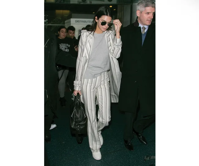 Person in a striped suit and sunglasses walking with a crowd at an indoor location.