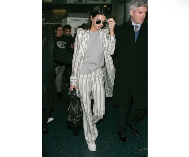 Person in a striped suit and sunglasses walking with a crowd at an indoor location.