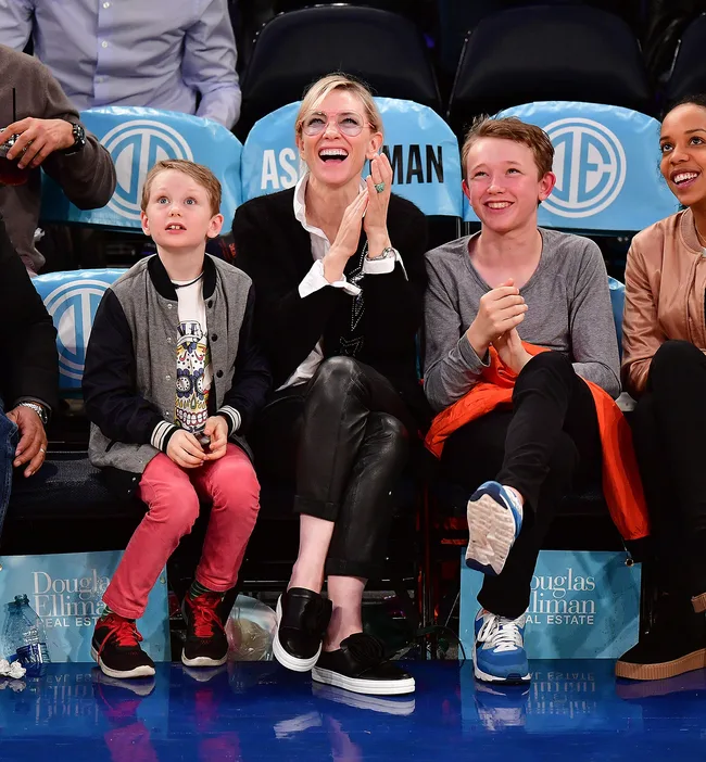 A woman and three children clapping and watching a basketball game from the front row seats.