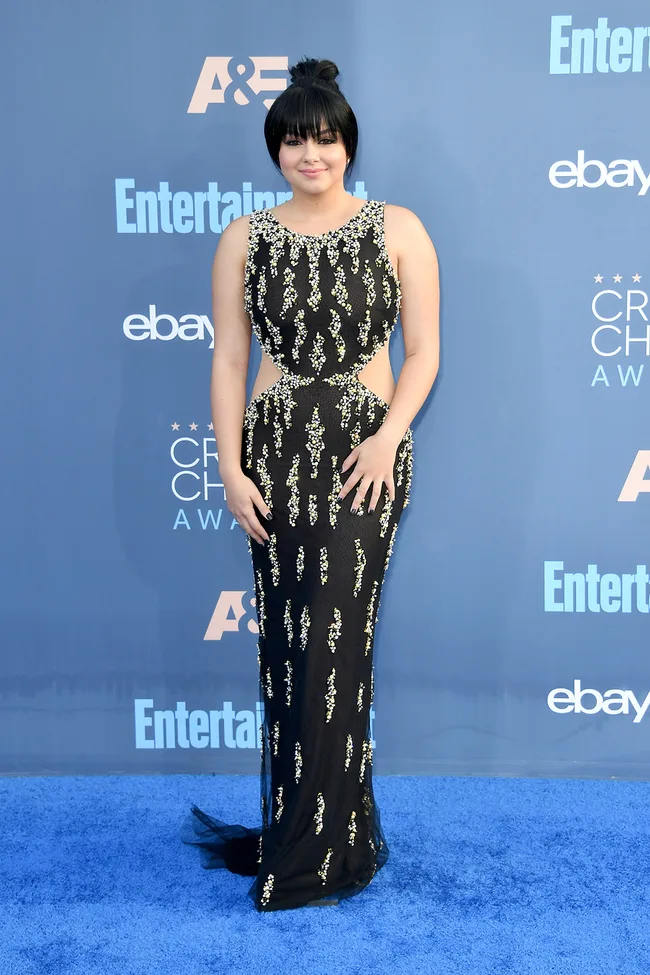 A person in a black dress with silver accents poses on the blue carpet at the Critics' Choice Awards event.