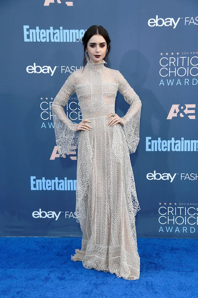 Woman in a lace gown poses on blue carpet at Critics' Choice Awards with Entertainment Weekly and eBay logos in background.
