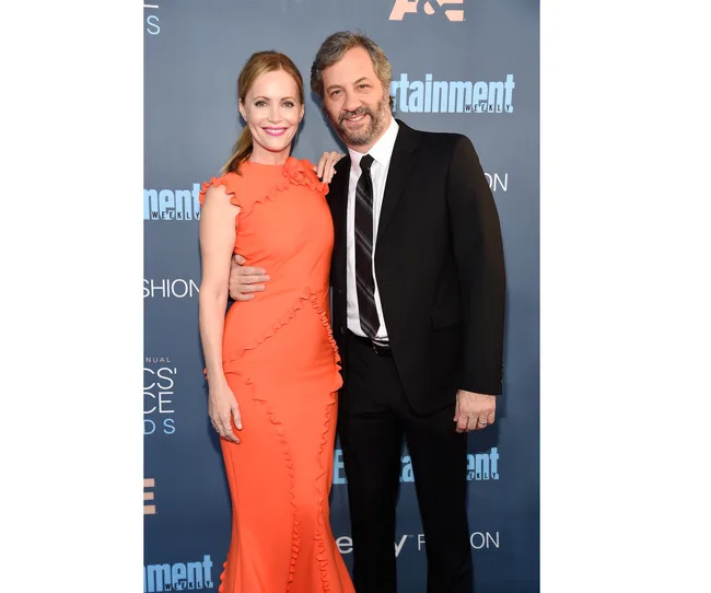 Man in a suit and woman in an orange dress posing on a blue carpet at an awards event.