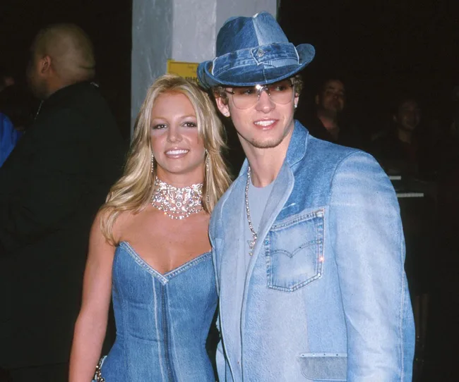 Two individuals wearing iconic matching denim outfits at a red carpet event.