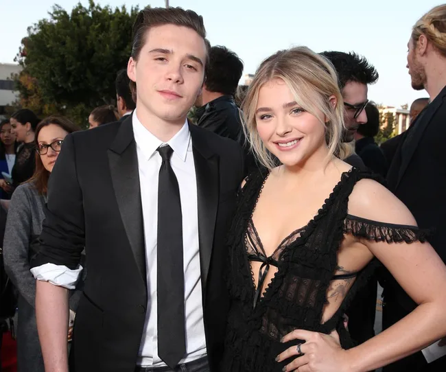 Young man in a black suit and woman in a black dress smiling together outdoors at an event.