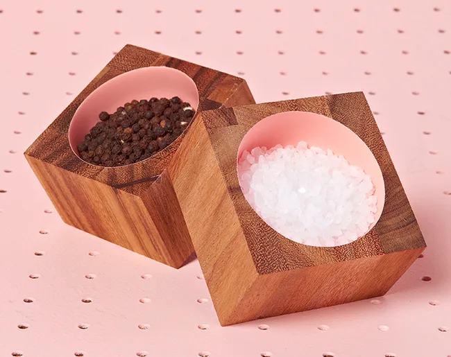 Wooden cubes with salt and pepper on a pink background.