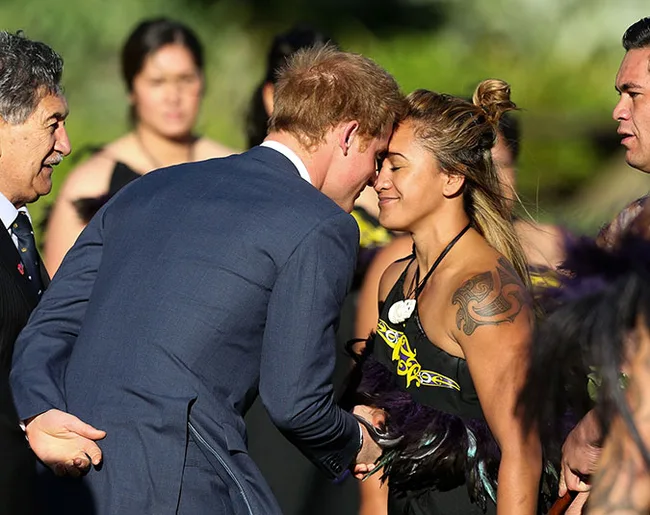 A person in a suit receives a traditional Maori hongi greeting from a woman in cultural attire.