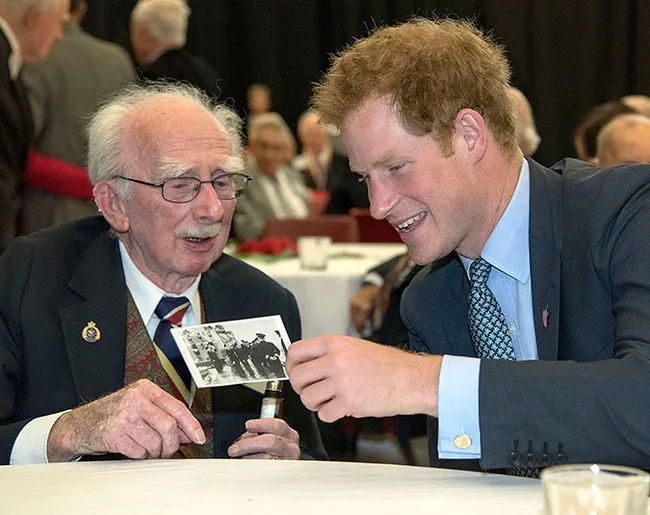 A man and an elderly war veteran smiling and looking at a black-and-white photo at an event.