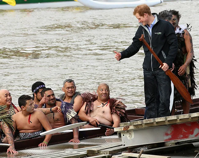 A person shakes hands with a group of traditionally dressed individuals in a boat near the water's edge.