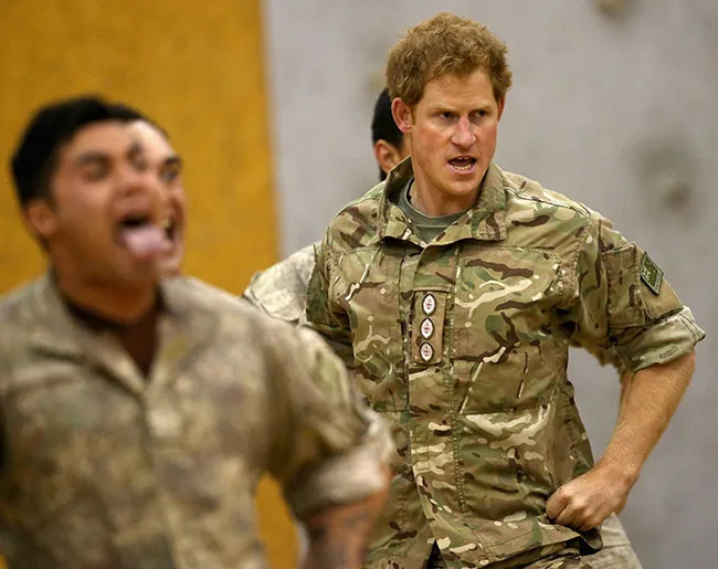 A man in camouflage uniform with a serious expression joins a military exercise, another participant is blurred in the foreground.