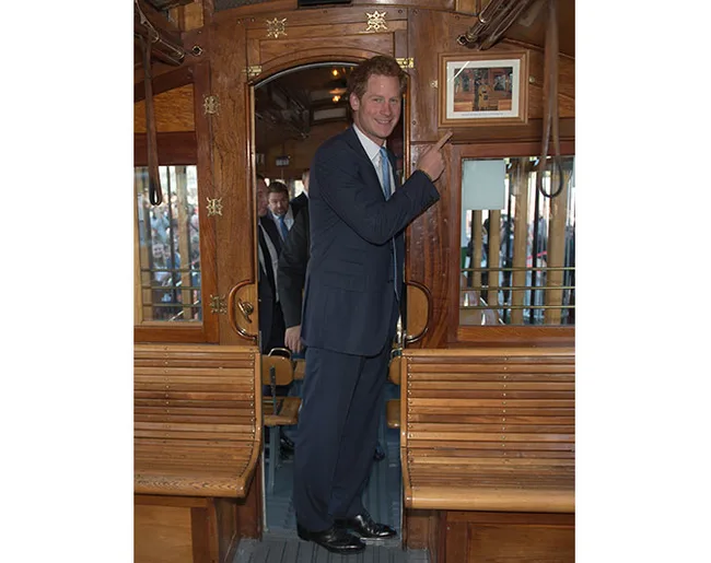 Man in a suit pointing at a framed picture inside a vintage-style wooden tram car.