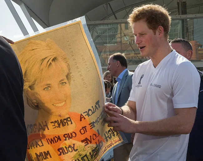 Man in a white shirt holds a poster with Princess Diana's portrait in an outdoor setting.