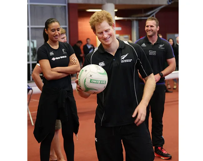 Man in black sports attire holding a rugby ball, smiling, with onlookers in a gym setting.