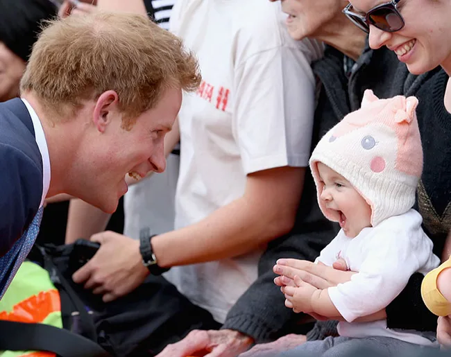 "A man smiling at an excited baby wearing a pink and white hat, surrounded by onlookers."