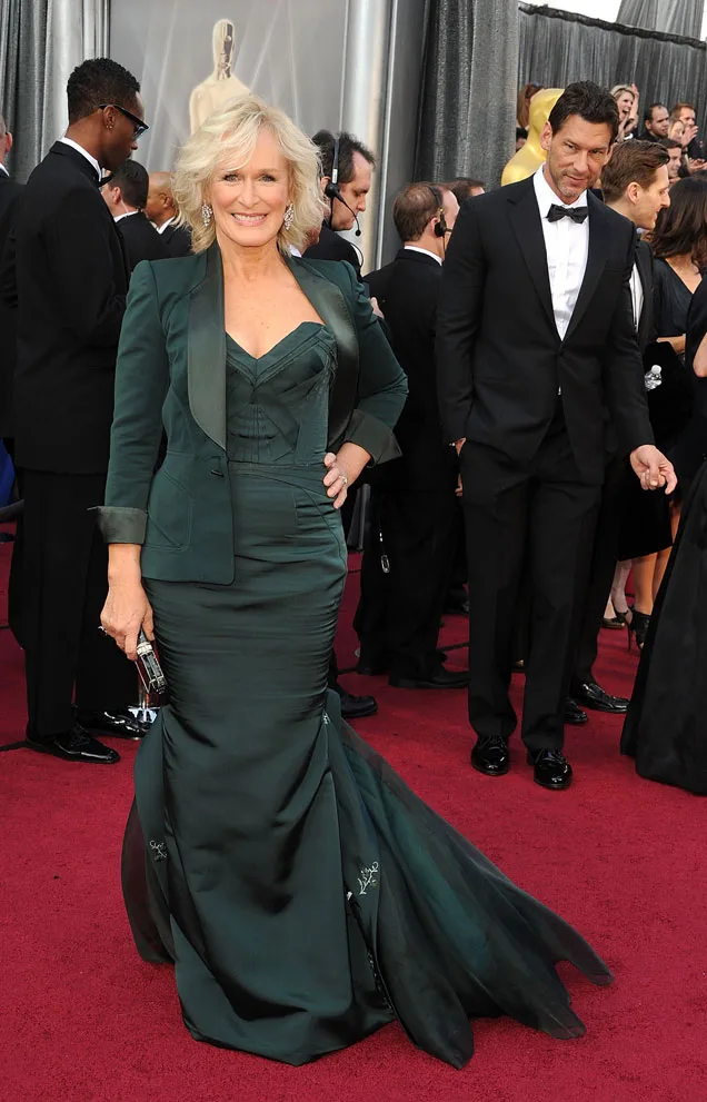 Elegant woman in a green gown on a red carpet, surrounded by attendees in formal attire.