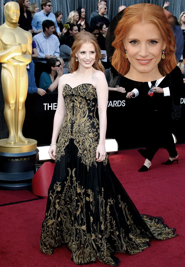 Red carpet event with woman in an elegant black gown with gold detailing beside an Oscar statue.