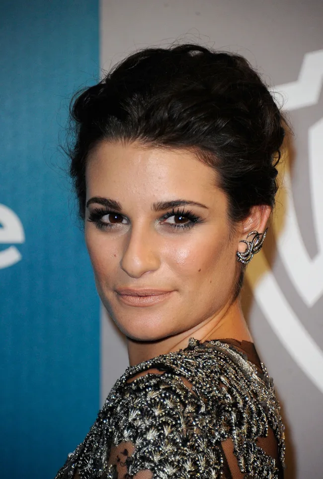 A woman with dark hair is wearing an ornate dress and earrings, looking back over her shoulder.