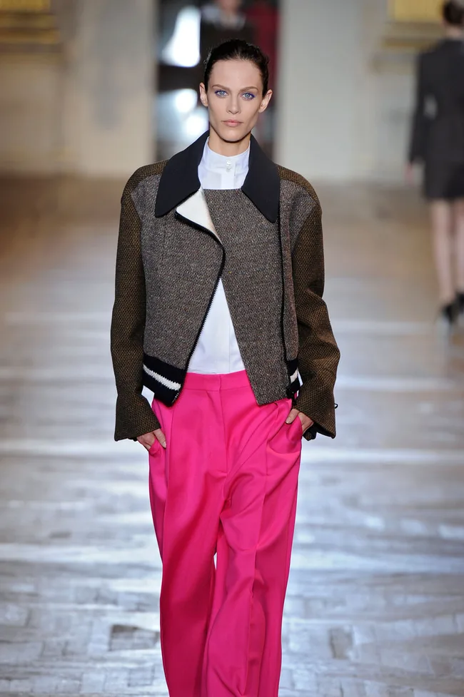 Model on runway in brown jacket and bright pink pants.