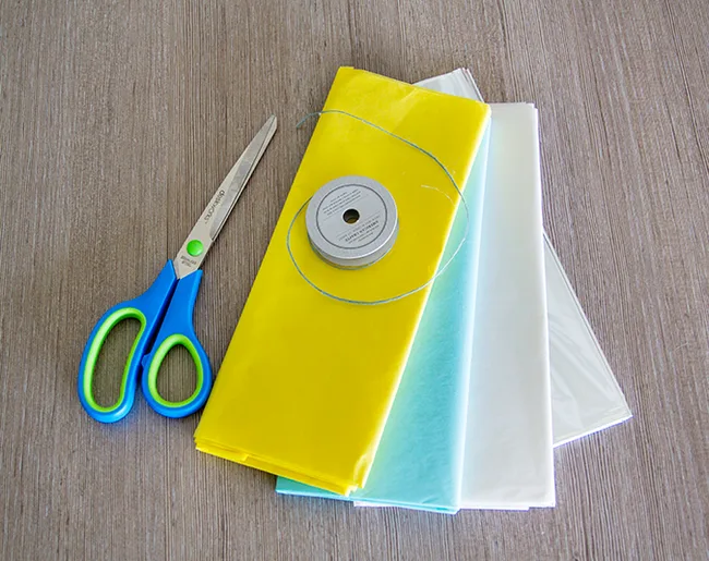 Scissors, yellow and blue tissue paper, white spool of thread on wooden table.