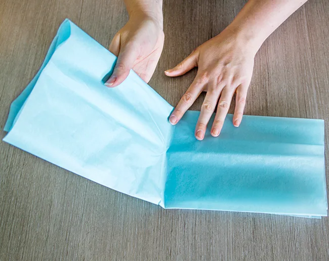 Hands folding blue tissue paper on a wooden table.