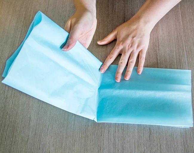 Hands folding blue tissue paper on a wooden table.
