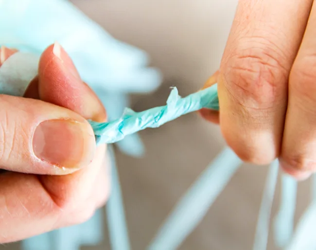 Close-up of hands twisting thin strips of blue plastic together.