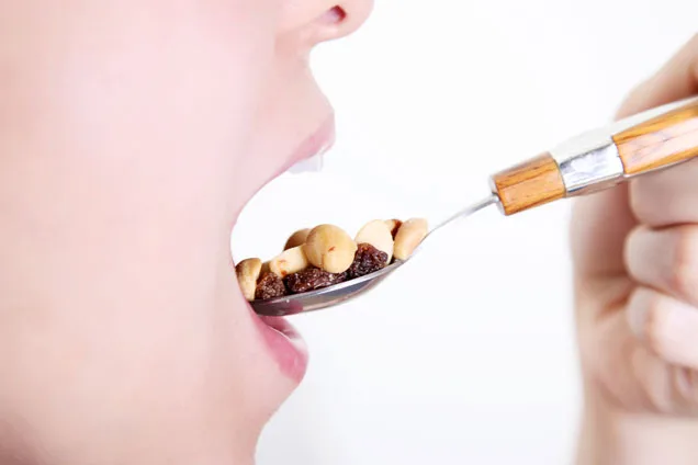 Close-up of a person eating a spoonful of nuts and raisins.