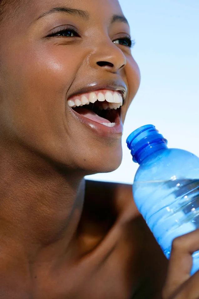 A person smiling while holding a blue water bottle with the cap open.
