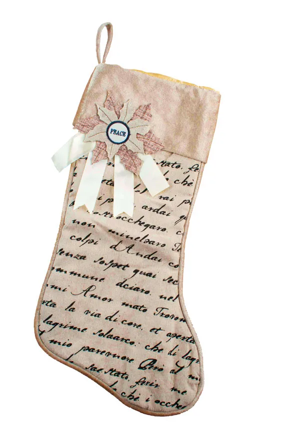 Cream Christmas stocking with cursive writing, lace accents, and a "Peace" decoration.