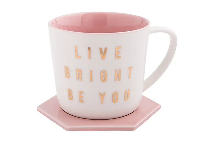 White mug with pink interior and coaster, gold letters reading "Live Bright Be You."