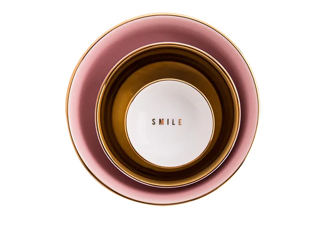 Three stacked plates; pink, gold, and white with "SMILE" on the white plate.
