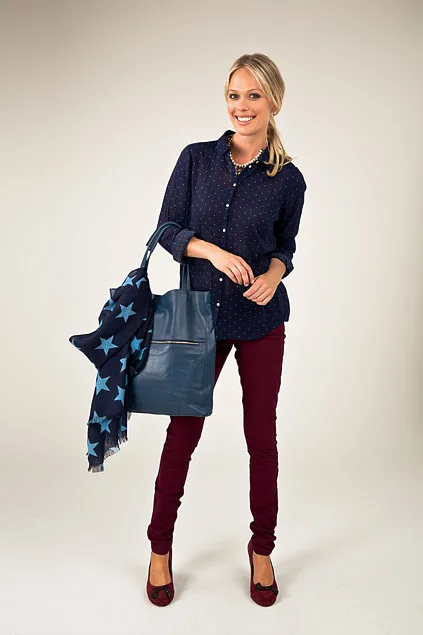 Woman smiling, wearing a navy blouse, burgundy pants, holding a blue bag with a star-patterned scarf.
