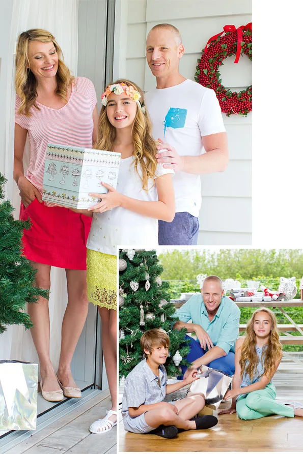 A family celebrating Christmas, standing by a wreath and Christmas tree, with a child holding a gift.
