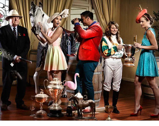 Group of people with horse, trophies, and derby-themed attire in an elegant room.