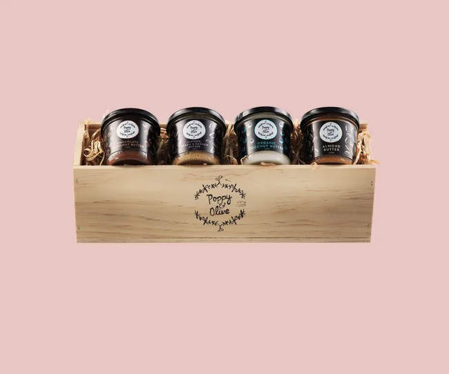 Gift box with four Poppy & Olive nut butter jars on a pink background.
