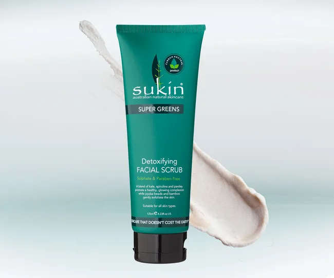 Sukin Super Greens Detoxifying Facial Scrub in a teal tube with a smear of the scrub on a light background.