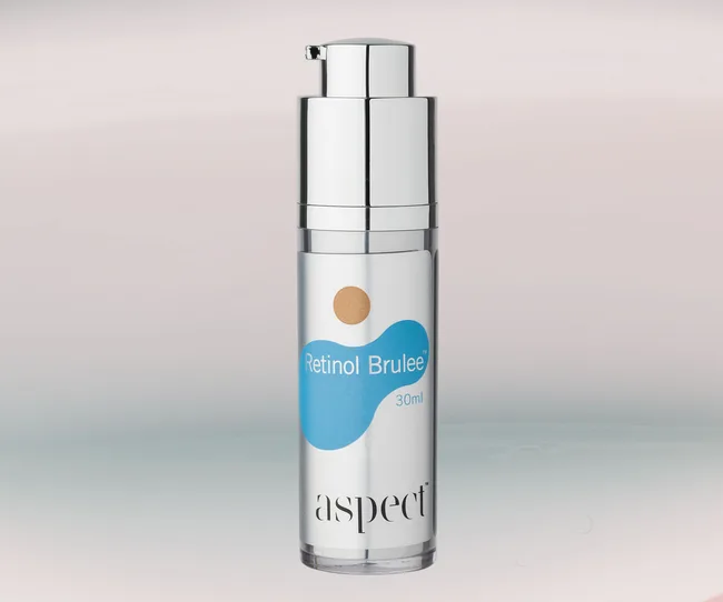 Bottle of Aspect Retinol Brulee, 30ml, with silver pump and blue label on a light background.